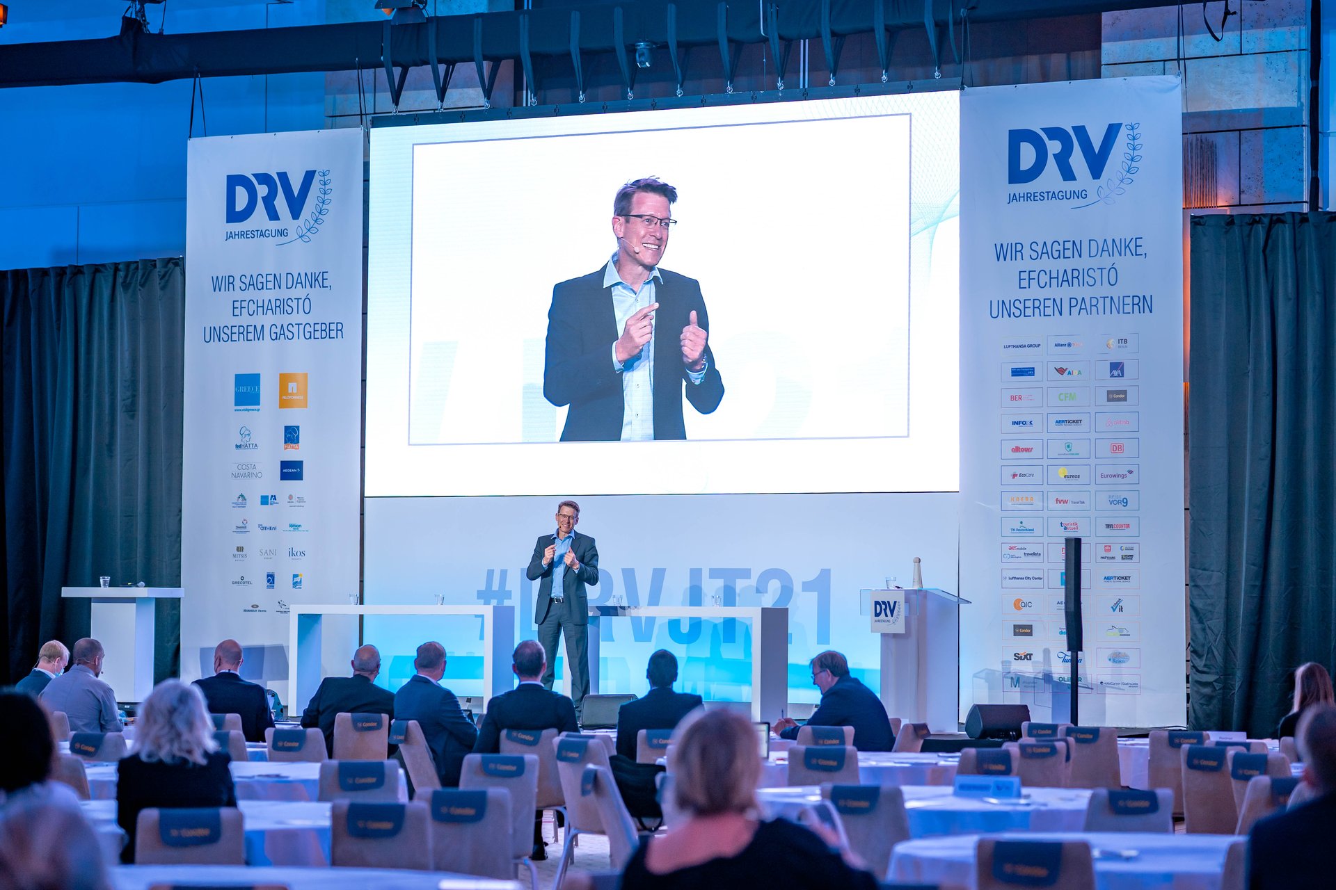 Harald Zeiss auf der DRV-Jahrestagung vor großem Saalpublikum, sein Gesicht auf der Leinwand